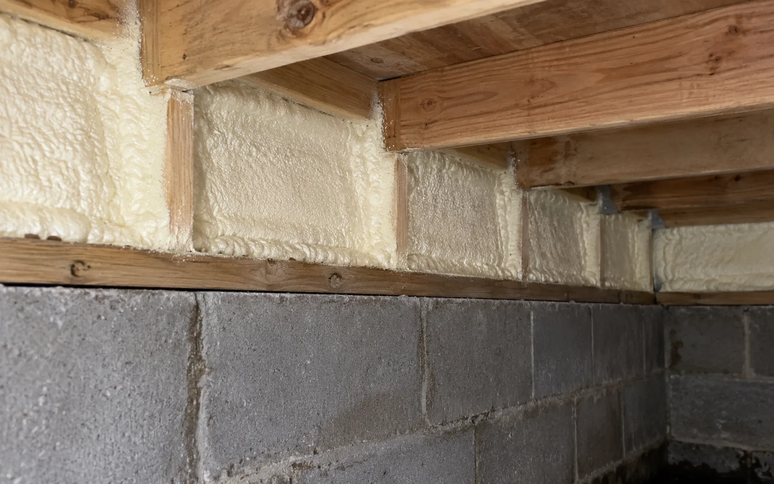 Closed-cell foam run along the rim joist between the floor joists, sealing the band above a block foundation