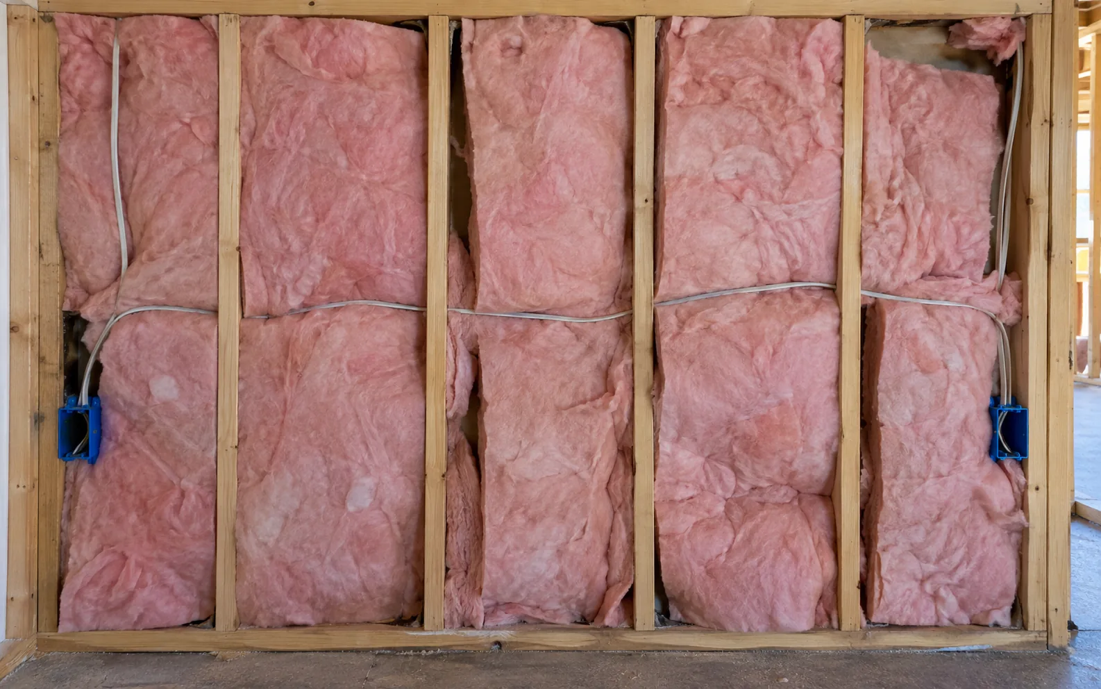 Batts stuffed into stud bays: compressed behind the wiring, bunched at the corners and left gapping at the edges