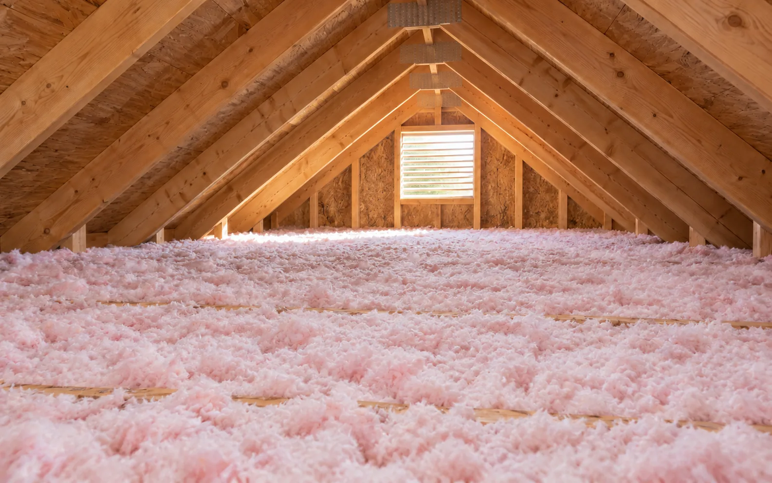 Pink loose-fill fiberglass blown to depth across the same attic floor